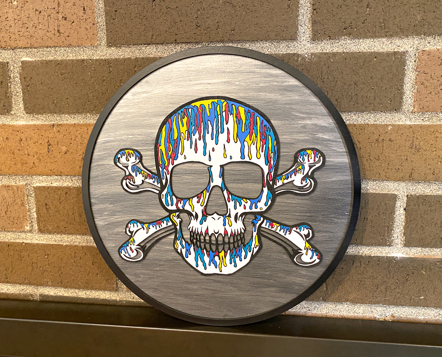 Colorful skull and crossbones design on a circular metal plate against a brick wall.