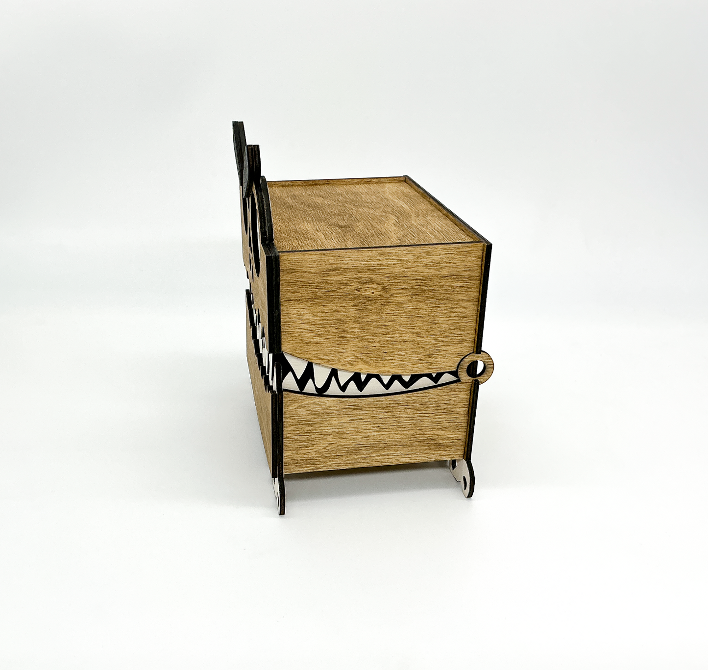 Side view of a walnut-stained wooden Monster Box showing its layered construction, small feet, and hinged lid. The googly eye and eyebrow are partially visible, highlighting the box’s quirky Halloween-themed design.