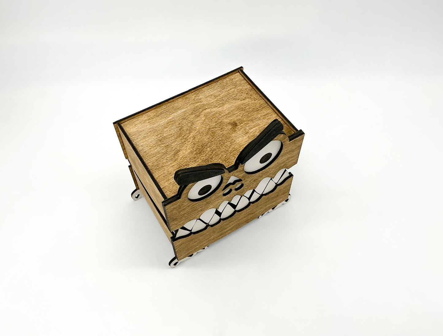 A top-down perspective of the handcrafted wooden monster box, stained in a rich walnut color. The hinged lid is closed, and the top portion of its playful googly eyes and fuzzy eyebrows can be seen peeking up from the front. The subtle texture of the birch wood is visible across the lid's surface.