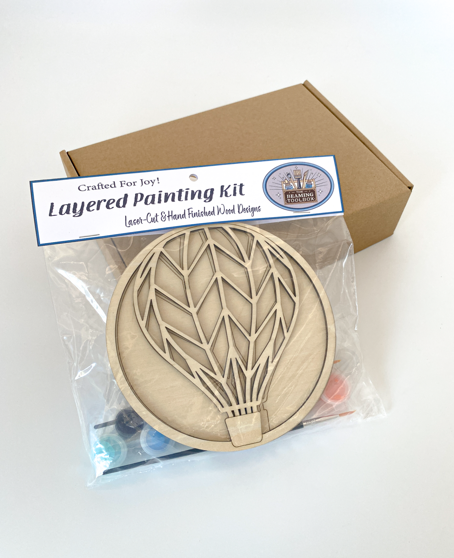 Layered painting kit with wooden hot air balloon design in clear packaging.
