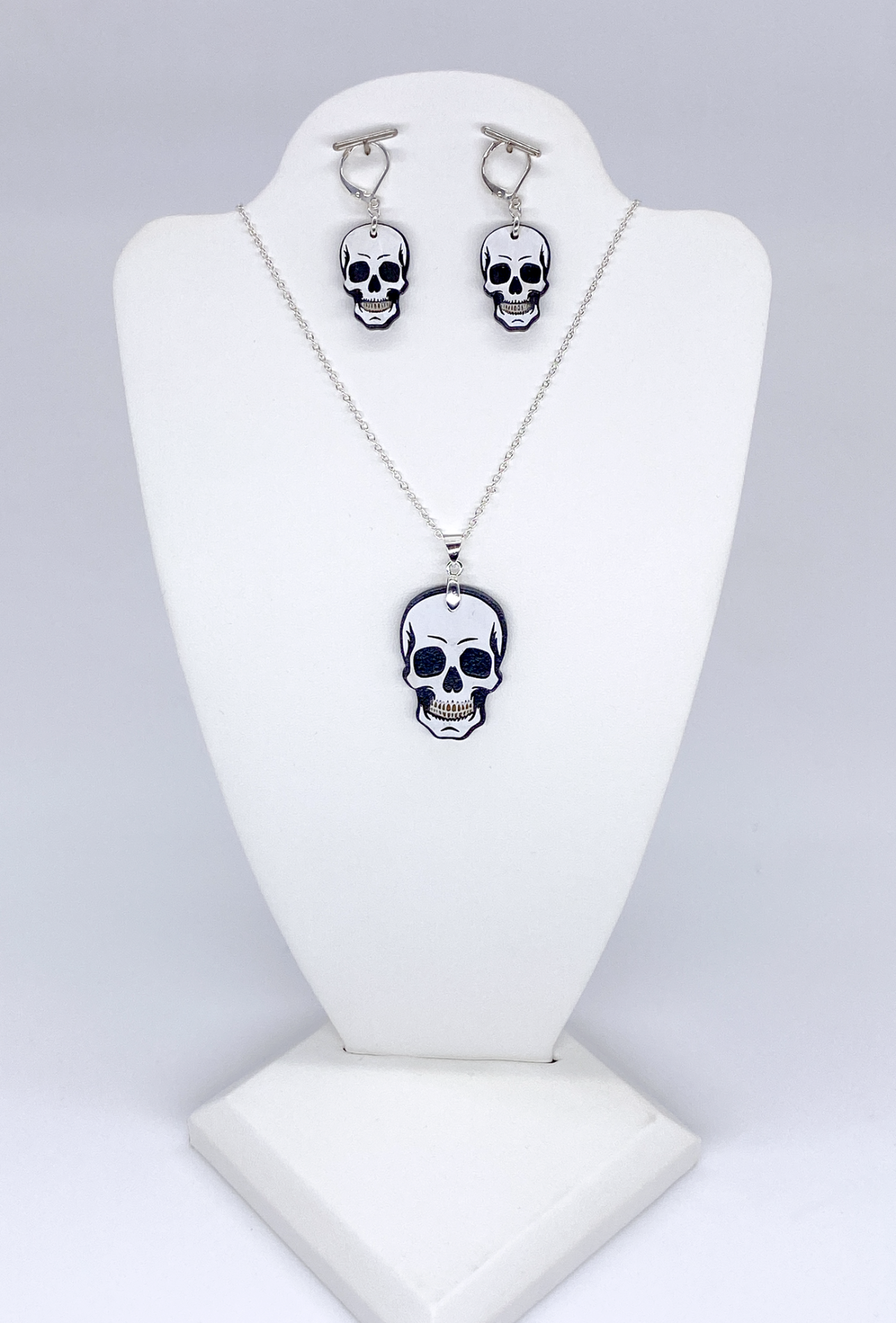 Skull-themed necklace and earrings set on a white stand against a light gray background