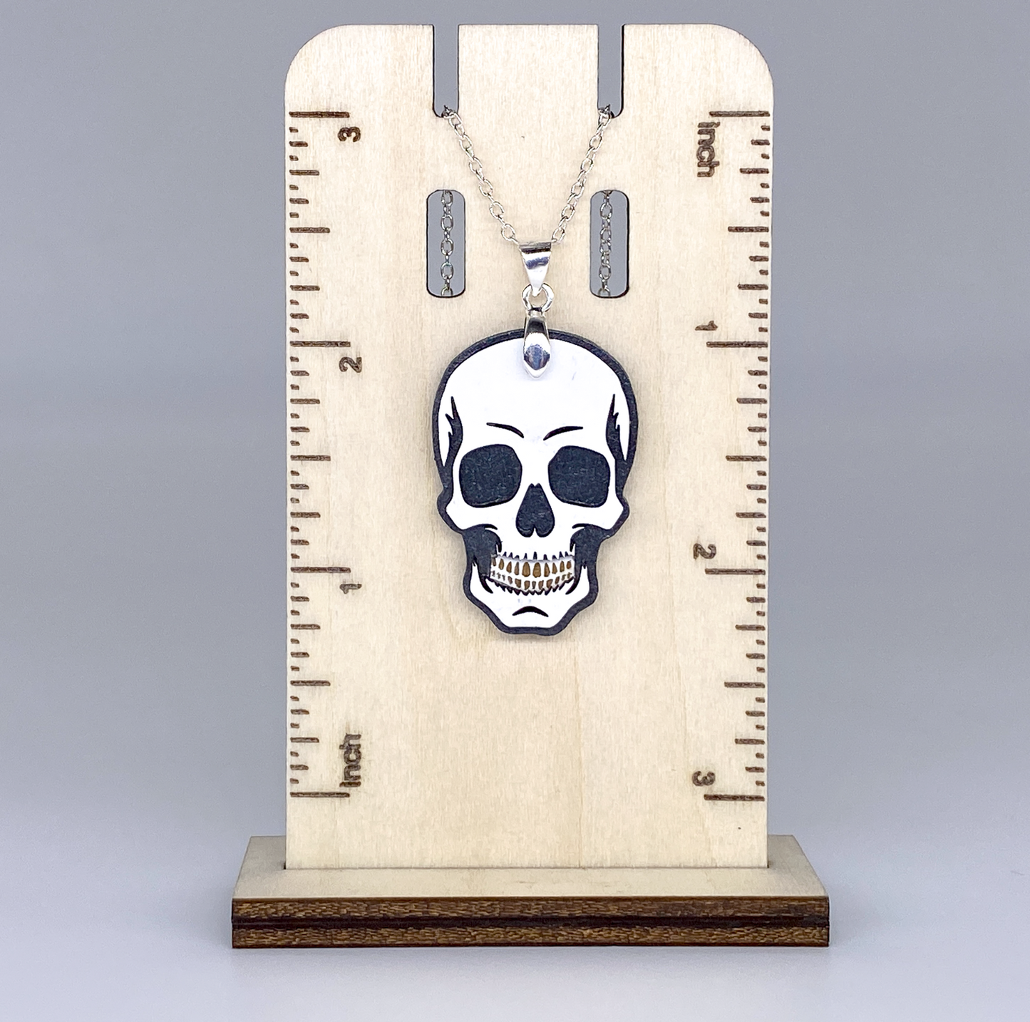 Skull pendant necklace on a wooden stand with measurement markings