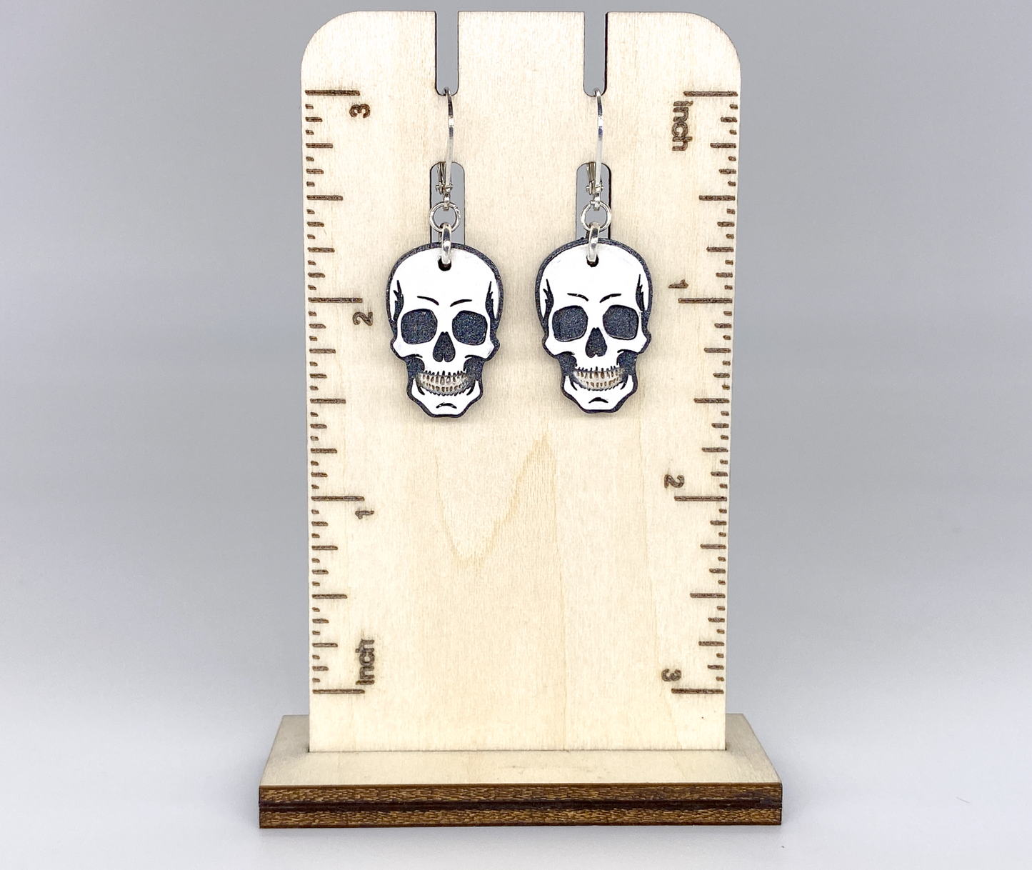 Skull-shaped earrings on a wooden stand with measurement markings.
