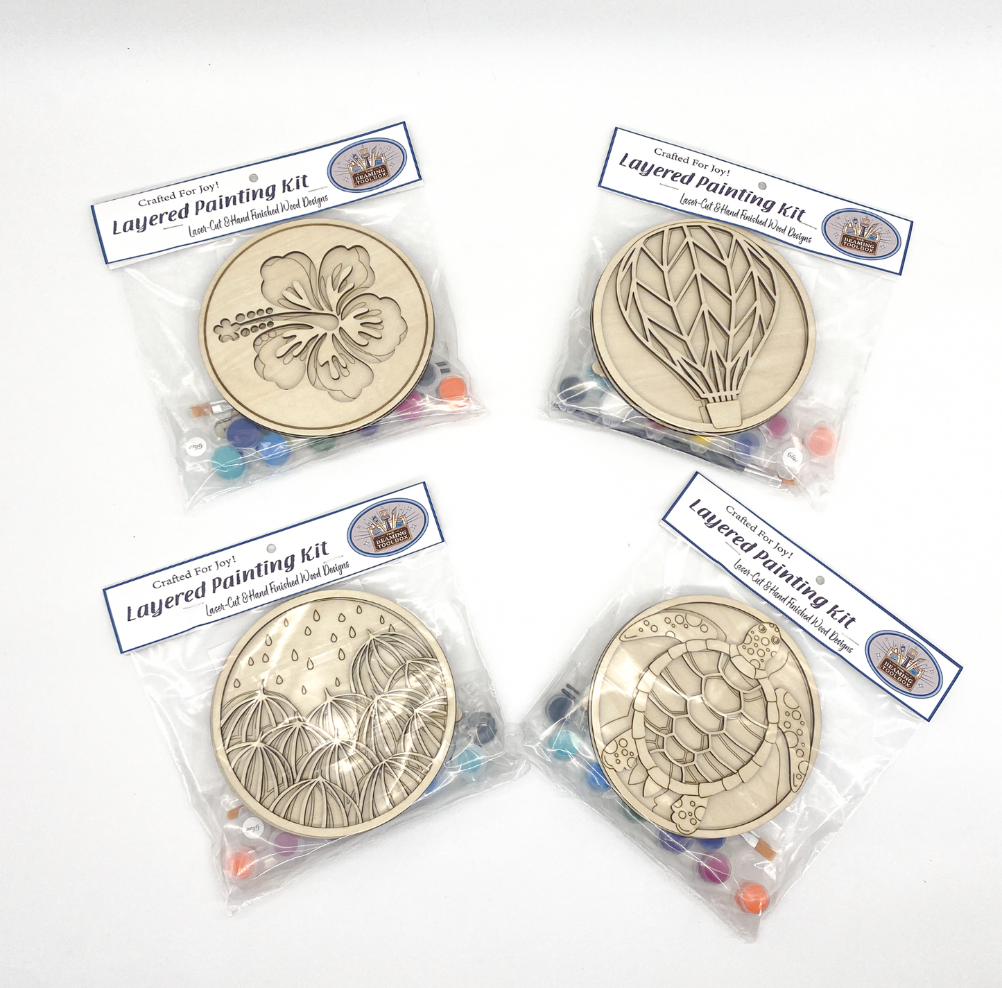 Four layered painting kits with designs on clear plastic packaging on a white background.