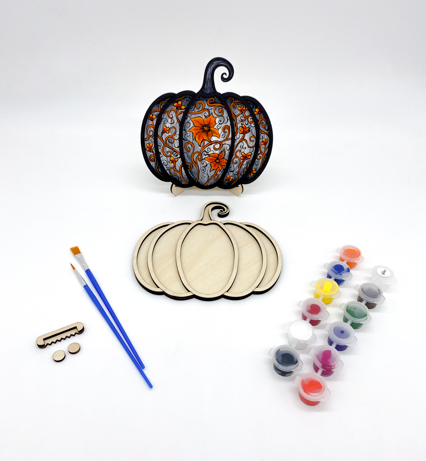 Decorative pumpkin cutouts with painting supplies on a white background