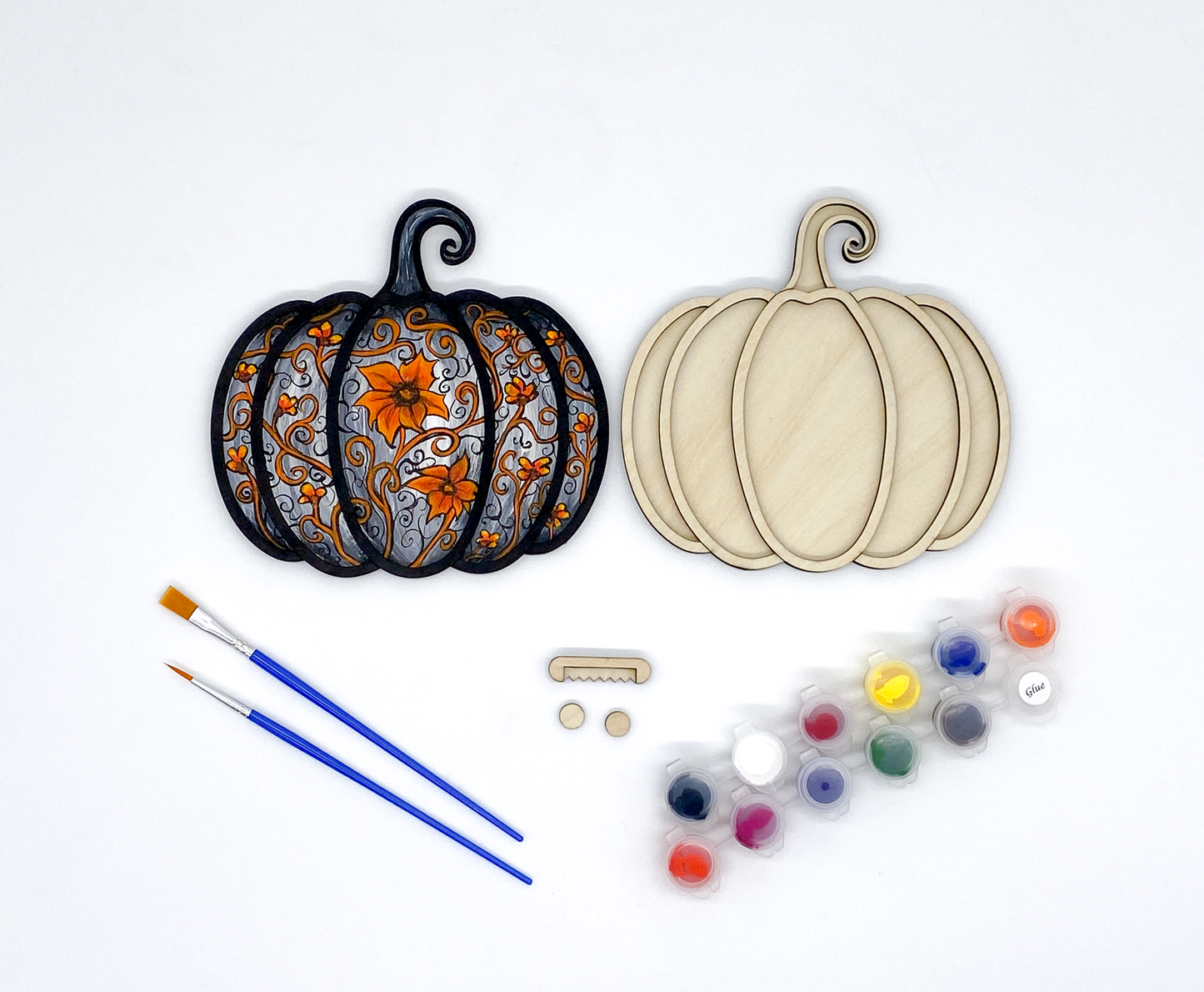 Decorative pumpkin cutouts with paint supplies on a white background