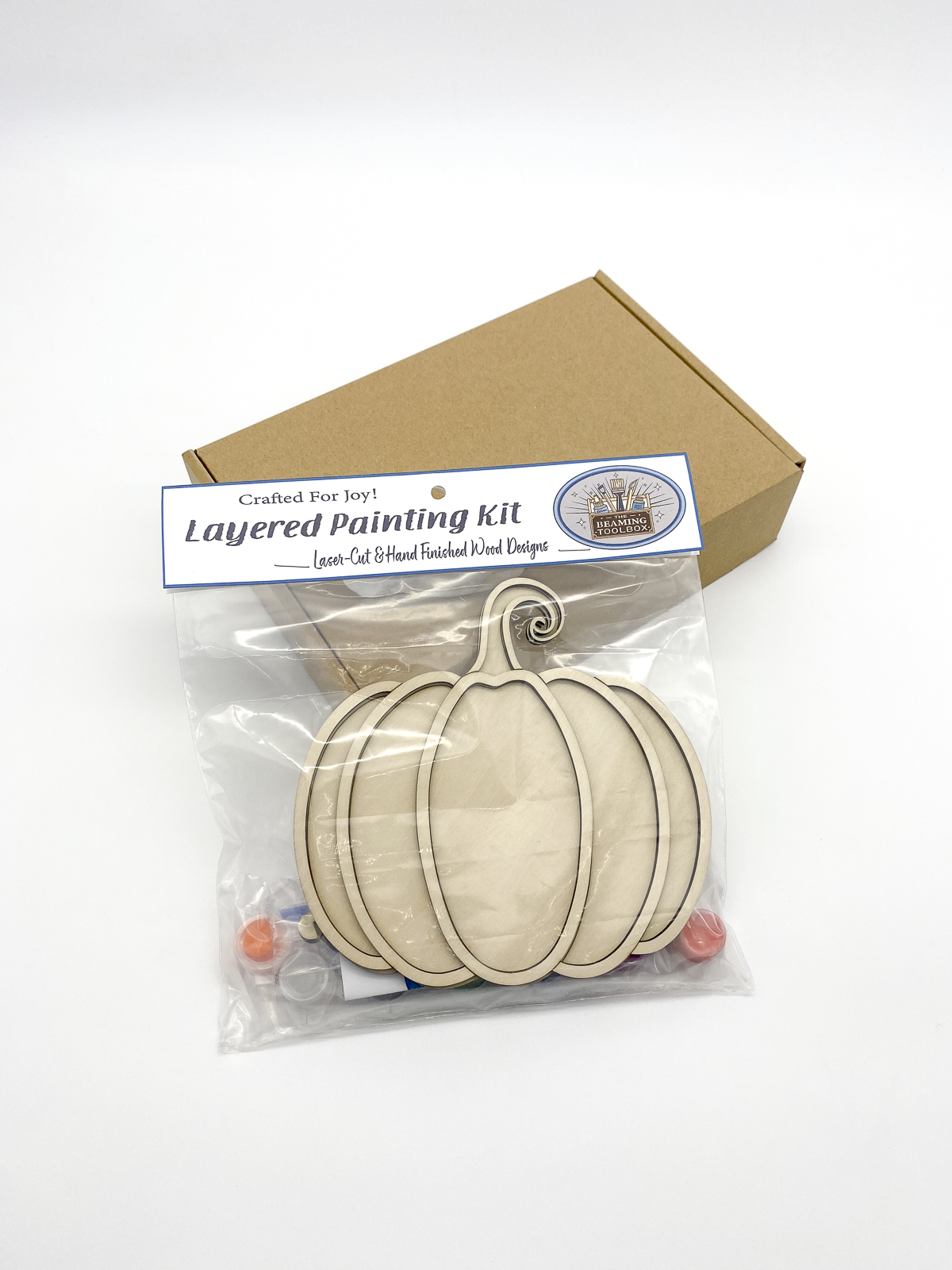 Layered painting kit with wooden shapes and packaging on a white background
