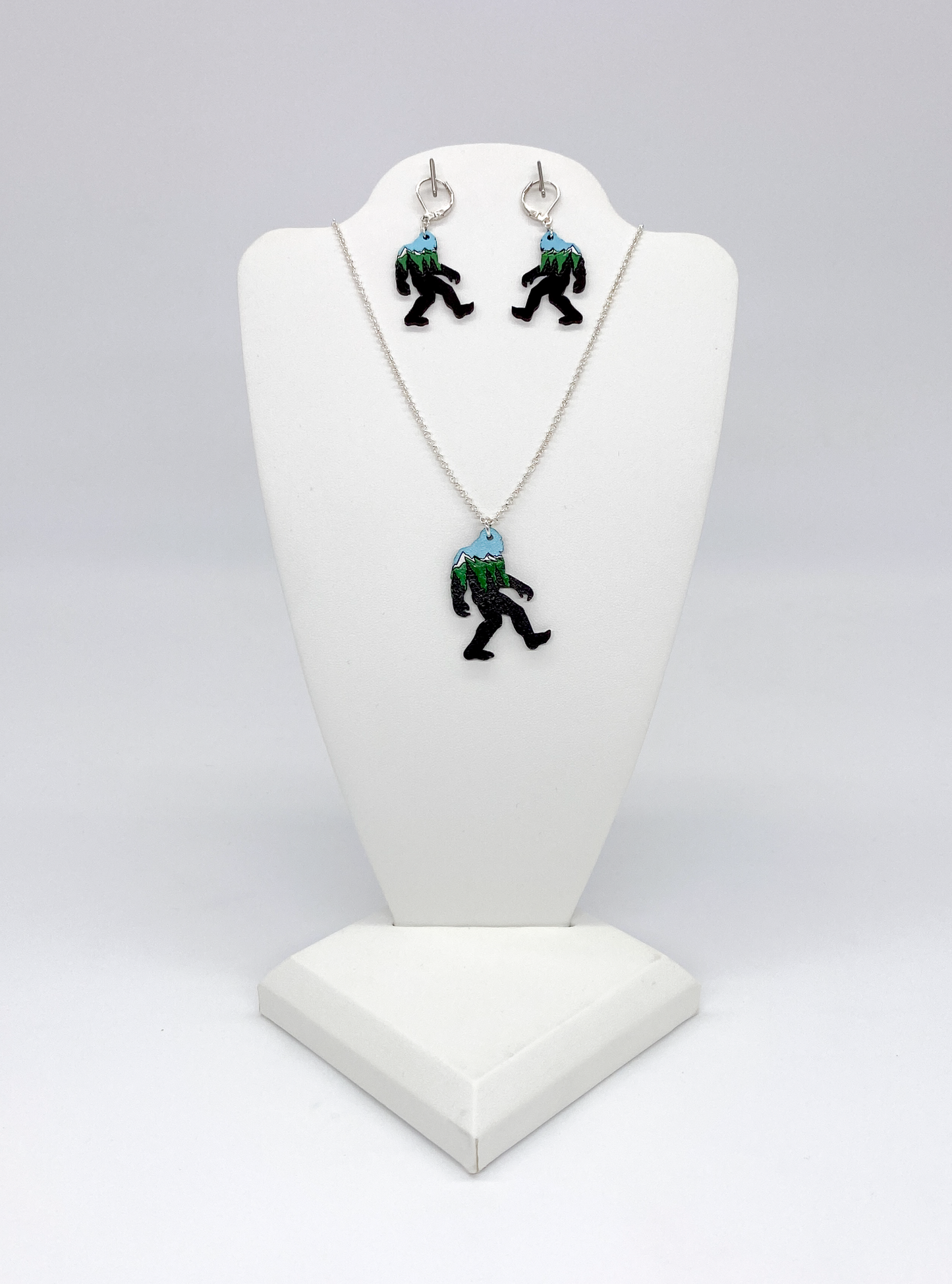 Bigfoot-themed necklace and earrings on a white bust