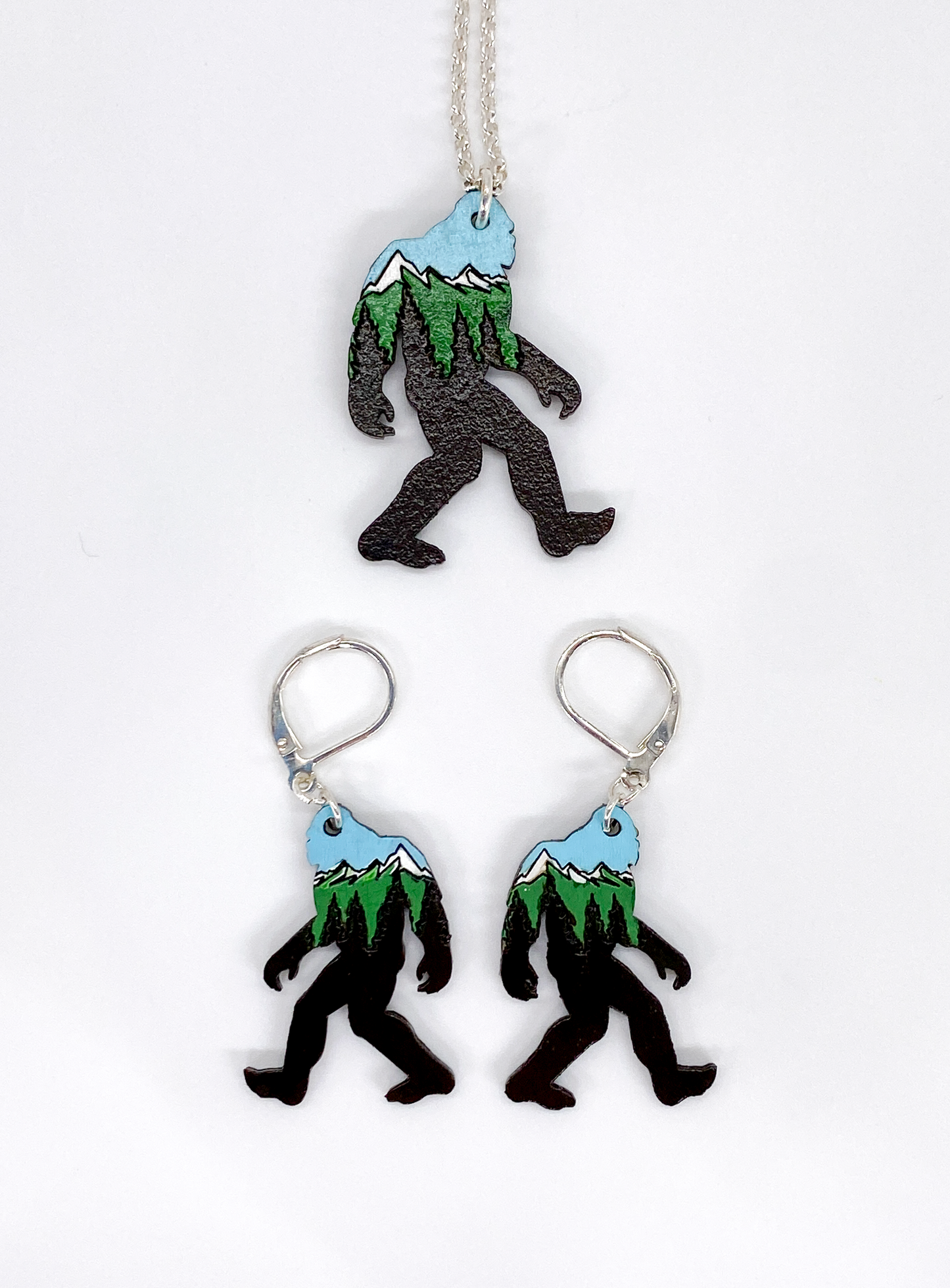 Sasquatch-shaped necklace and earrings with mountain designs on a white background