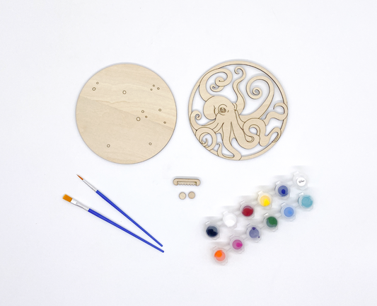 Wooden craft kit with circular wooden pieces, paintbrushes, and paint palette on a white background