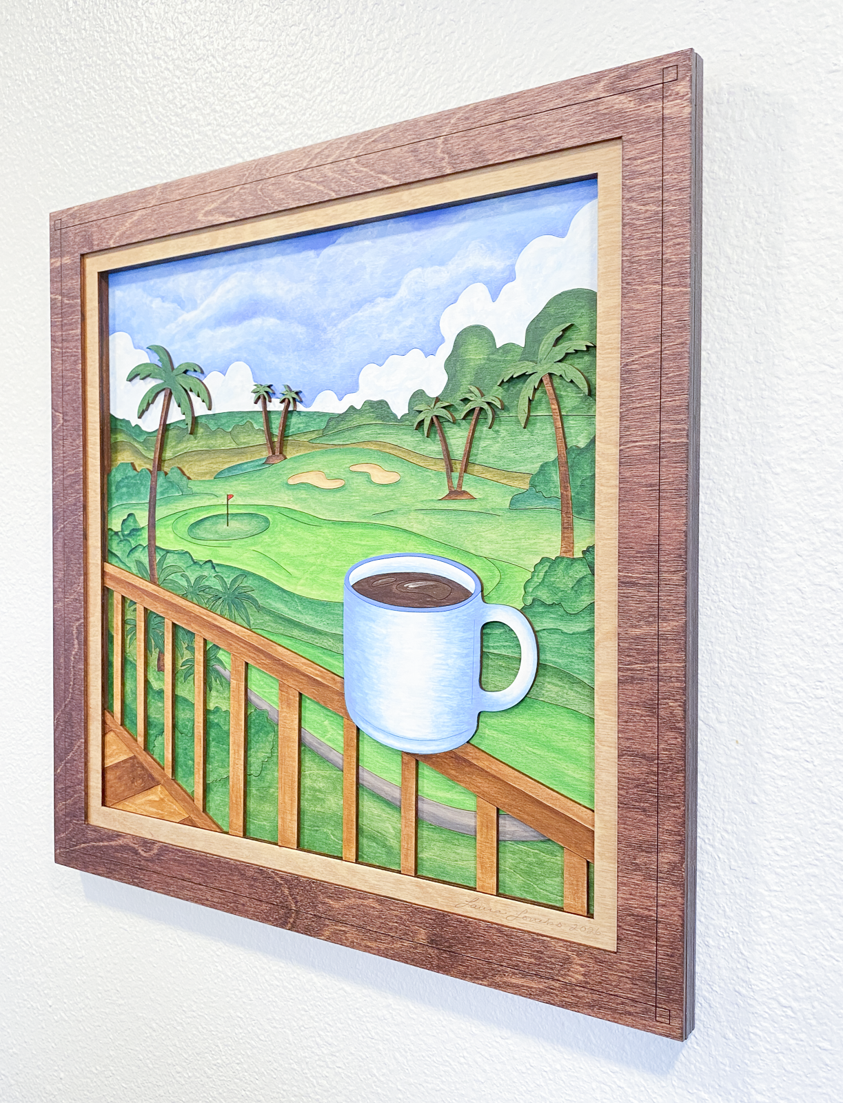 Lanai Mornings layered wood artwork displayed on a neutral wall, showing scale and custom stained wood framing surrounding the tropical golf course and coffee cup scene.