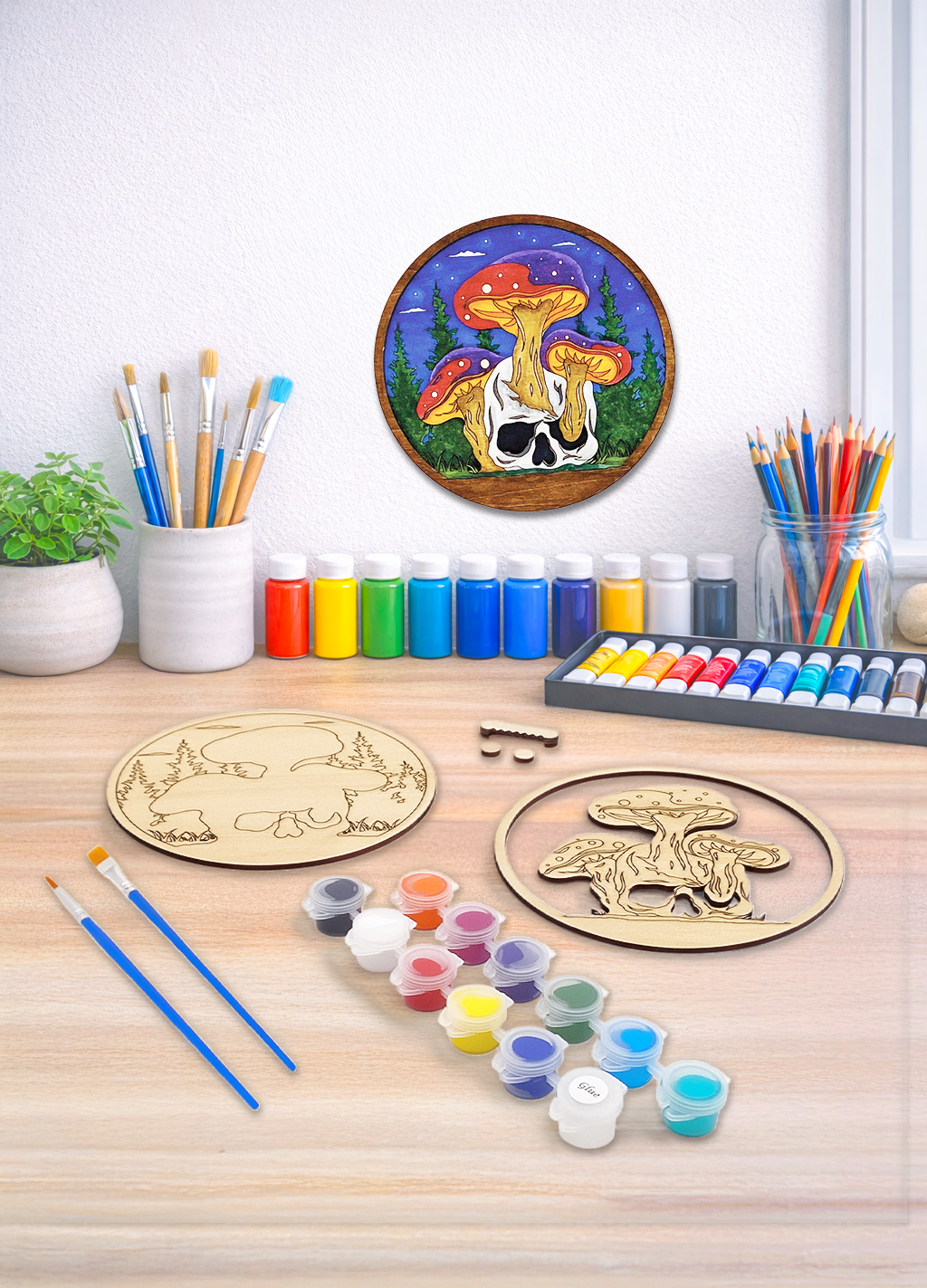 A 3D layered wood kit featuring a skull and mushroom design with paint pots and brushes for a DIY art project.