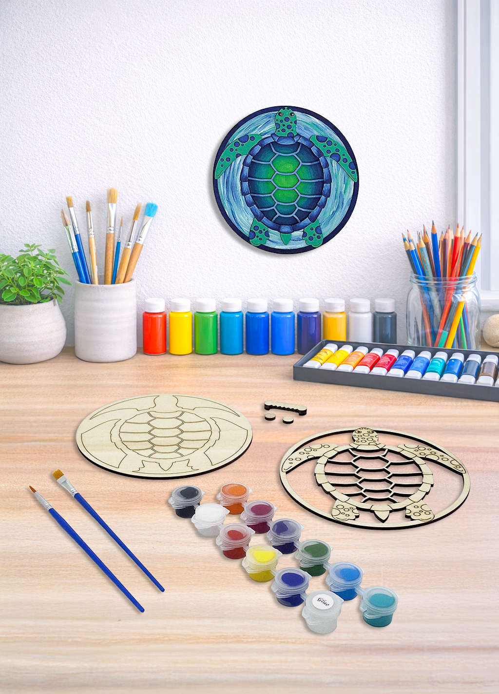 A 3D layered sea turtle wood art kit with 12 paint colors and brushes on a wooden tabletop workspace.