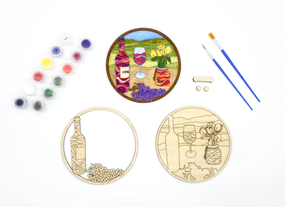 Complete DIY craft kit featuring painted wine art next to blank wood layers, paint pots, brushes, and hanging hardware