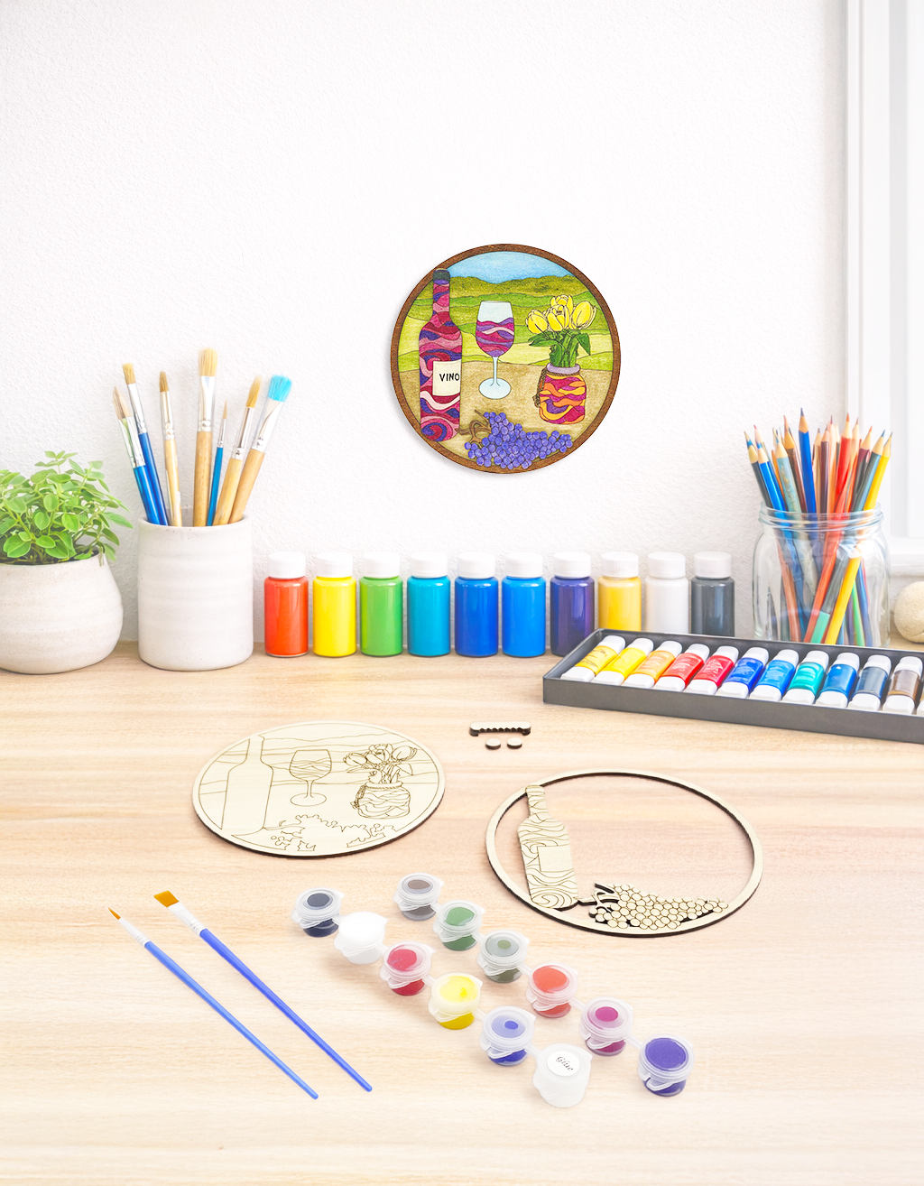 A creative maker’s desk with the unpainted wine kit, brushes, and art supplies, featuring the finished kit hanging on the wall above