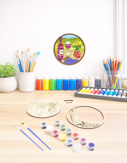 A creative maker’s desk with the unpainted wine kit, brushes, and art supplies, featuring the finished kit hanging on the wall above