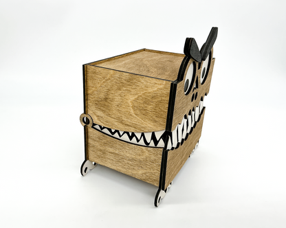 Side view of a walnut-stained wooden Monster Box showing its layered construction, small feet, and hinged lid. The googly eye and eyebrow are partially visible, highlighting the box’s quirky Halloween-themed design.