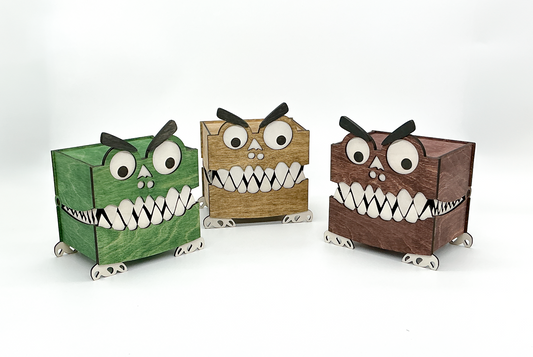 Three handcrafted Monster Boxes in walnut, mahogany, and green stains are lined up with their mouths closed, showing googly eyes, bushy eyebrows, and little feet. Their quirky, toothy grins and playful design make them perfect for Halloween decor or spooky-themed storage.