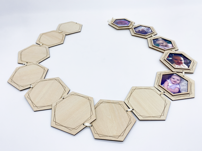 A wooden photo garland with a geometric design. The garland is made of connected hexagonal wooden frames, some holding baby photos. The frames are connected with cream colored string.
