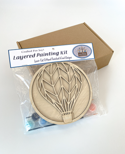 Layered painting kit with wooden hot air balloon design in clear packaging.