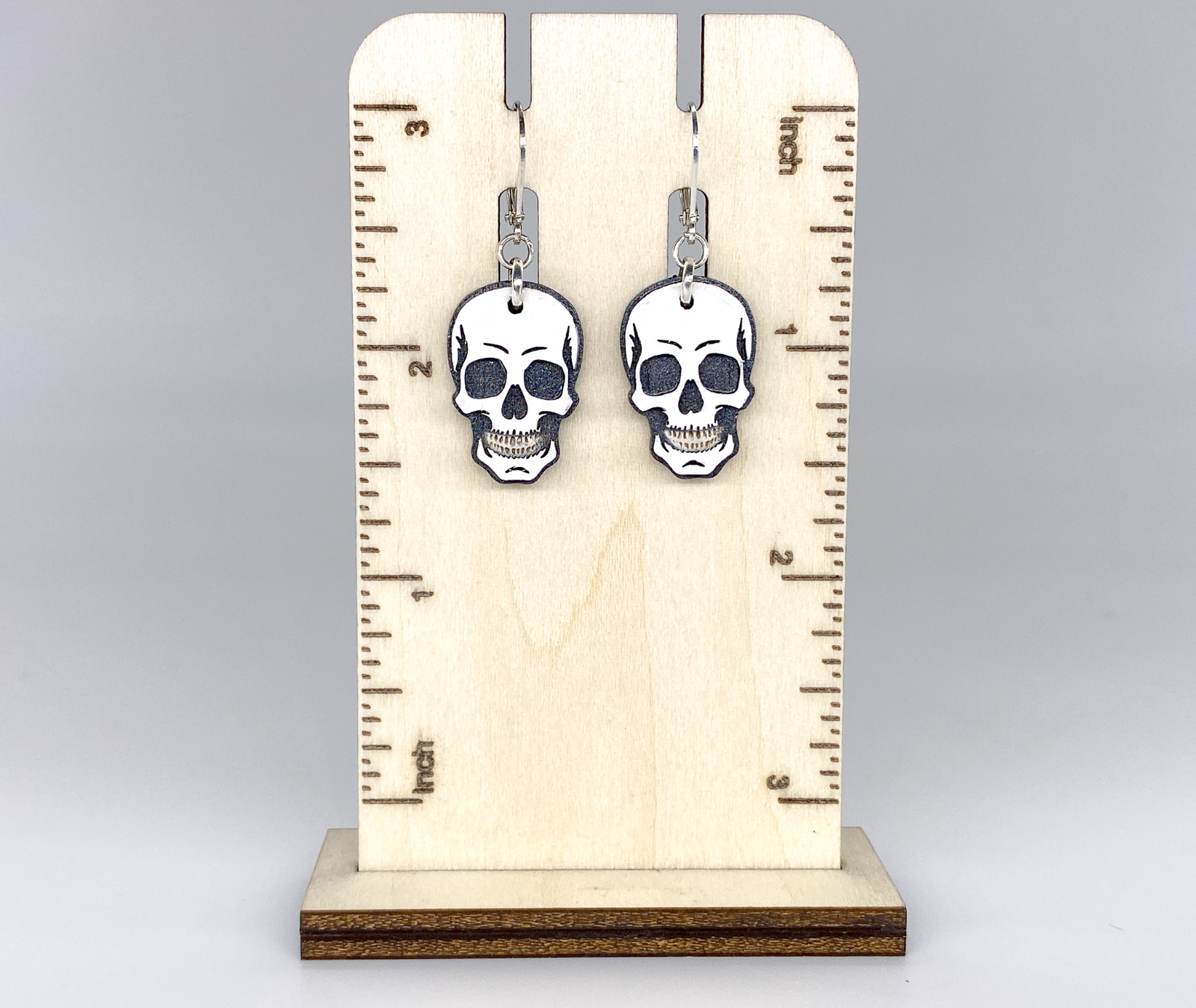 Skull-shaped earrings on a wooden stand with measurement markings.