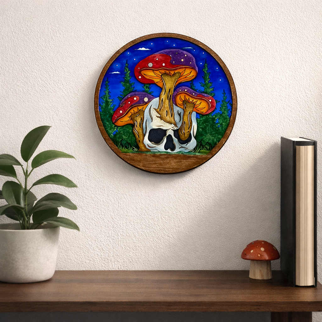 Mushroom and Skull Layered Wood Art kit completed and displayed on a white wall above a bookshelf with a plant