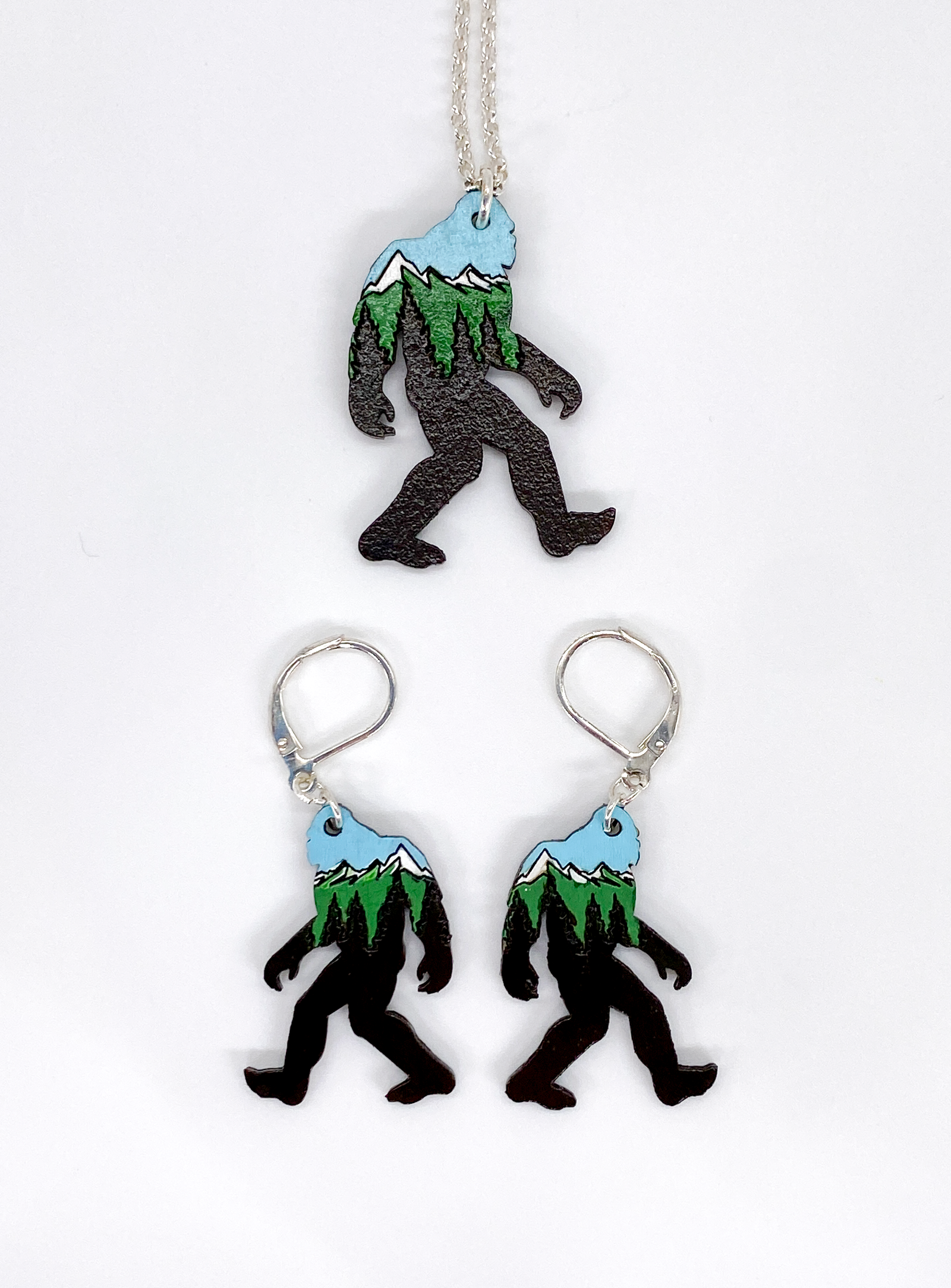 Sasquatch-shaped necklace and earrings with mountain designs on a white background