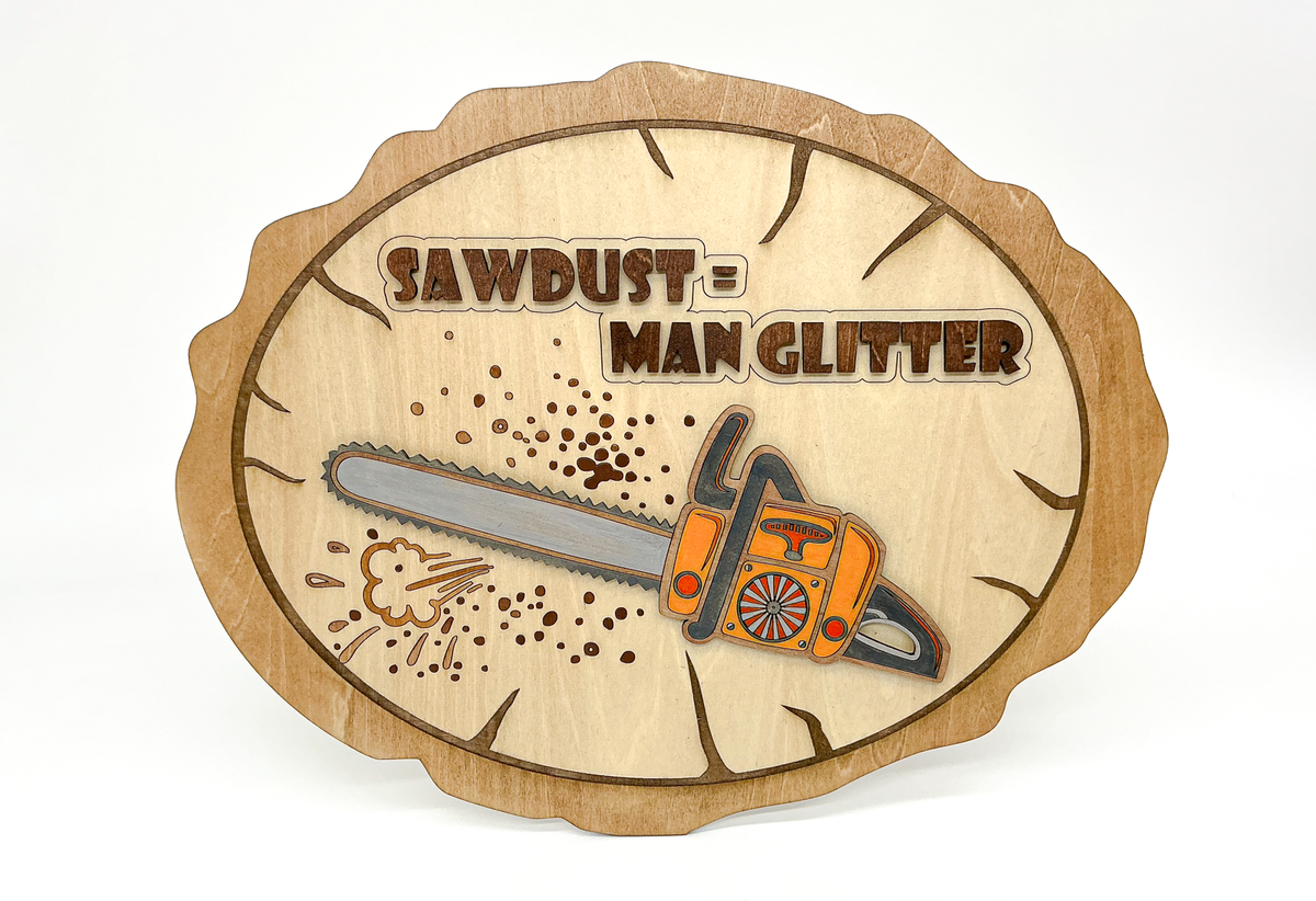 Front view of laser-cut wooden “Sawdust = Man Glitter” wall art featuring a dimensional orange chainsaw and engraved sawdust details.