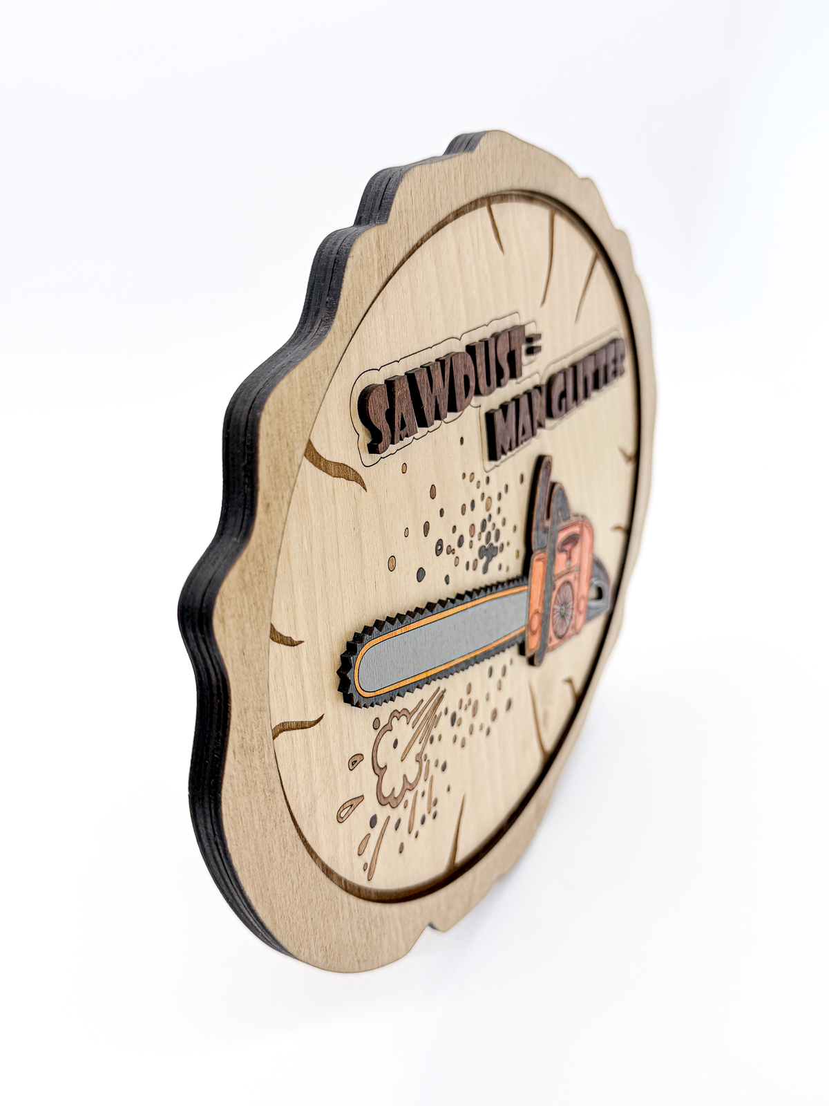 Angled side view of layered laser-cut wood wall art with a chainsaw design and “Sawdust = Man Glitter” text, showing the dimensional wood layers.