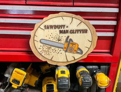“Sawdust = Man Glitter” layered wood chainsaw sign displayed on a red tool chest above yellow power tools.