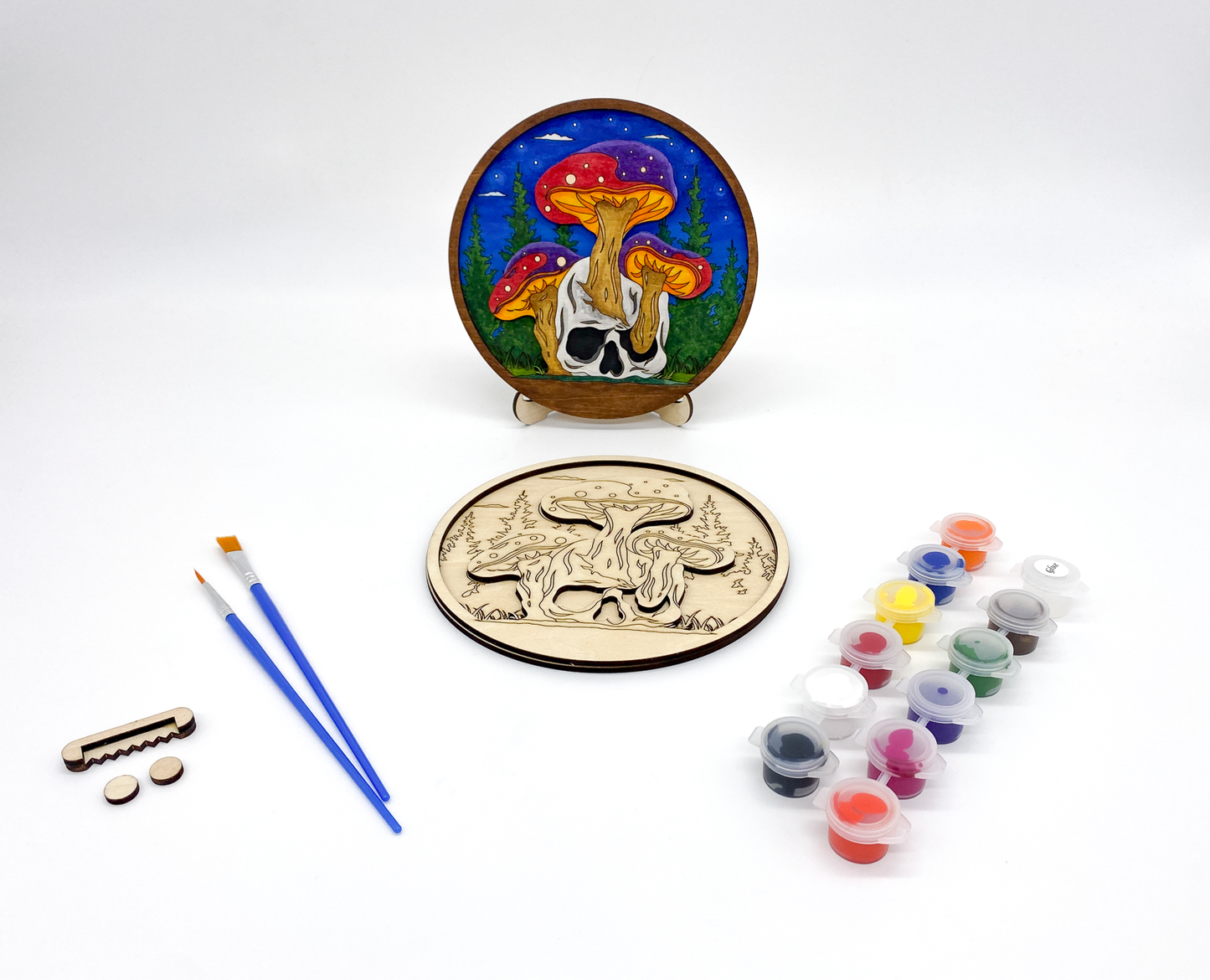 Mushroom and Skull Layered Wood Art kit, showing both layers combined and a completed version of the kit, sawtooth hanger and bumers, two paint strips and two paint brutshes.