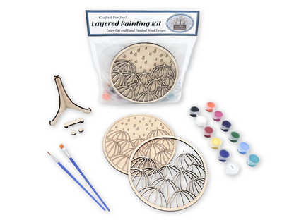 Umbrella painting kit for adults shown with packaged kit, unpainted layered wood pieces, paint pots, brushes, glue, and display stand.