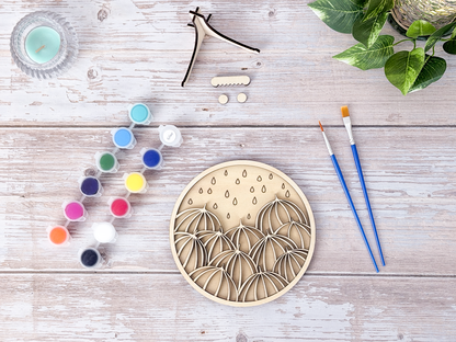 Umbrella unique wall art kit flat lay with unpainted wood layers, colorful finished example, instruction card, paint pots, brushes, glue, and stand pieces.