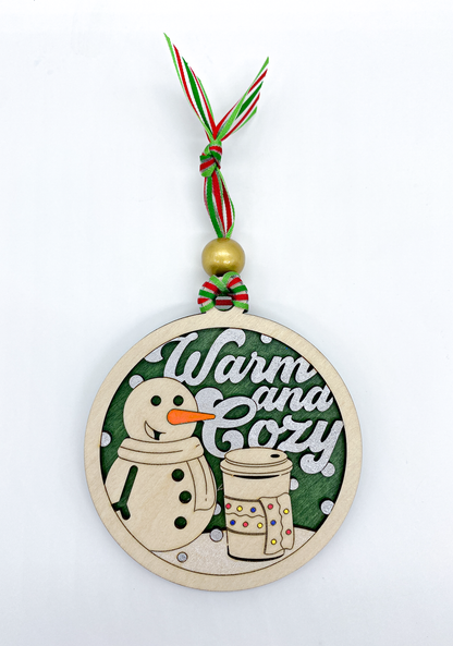 Decorative Christmas ornament with a snowman and text 'Warm and Cozy' on a white background.