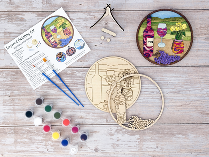 Wine and tulips DIY craft kit flat lay with finished painted example, unpainted wood layers, instruction card, paint pots, brushes, glue, and stand pieces.