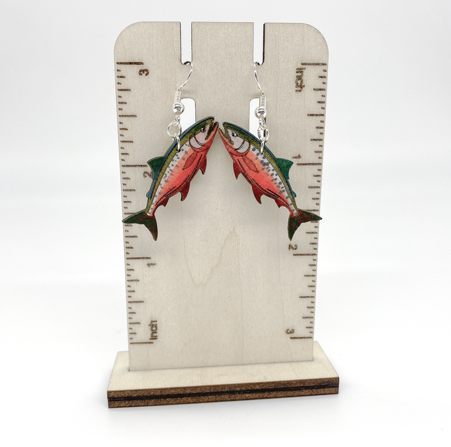 Salmon-shaped earrings on a wooden stand with measurement markings.