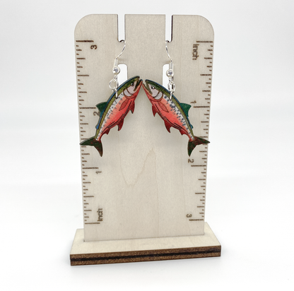 Salmon-shaped earrings on a wooden stand with measurement markings.