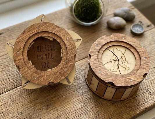 Two wooden Sasquatch trinket boxes showing the engraved Bigfoot lid and hidden “I Believe in You Too” message, displayed on a wooden table.