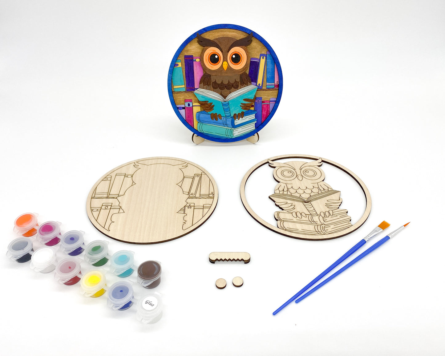 Wooden owl craft kit with paint, brushes, and unpainted pieces on a white background