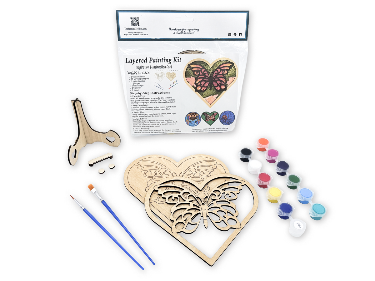 Butterfly heart layered wood painting kit in packaging with unfinished wood pieces, paint pots, brushes, glue, and display hardware.