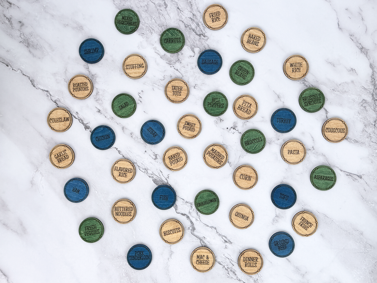 Assortment of color-coded wooden dinner planning coins with blue proteins, green vegetables, and brown side dishes.
