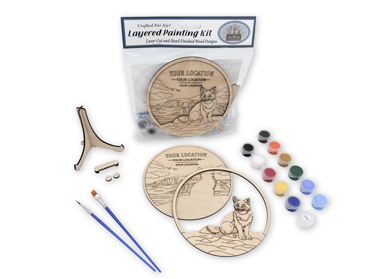 A layered wood carving and painting kit displayed on a white background, including a packaged kit labeled 'Crafted For Joy Layered Painting Kit', a laser-cut wooden design with a fox illustration, two round wooden panels, two small paintbrushes, a stand, and multiple small paint pots.