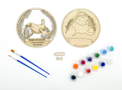 Custom sea lion DIY paint kit styled in coastal setting with craft supplies and finished piece displayed