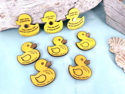 Personalized yellow wooden cruise ducks arranged on a light blue background with driftwood and seashells, showing engraved cruise details and magnetic versions.