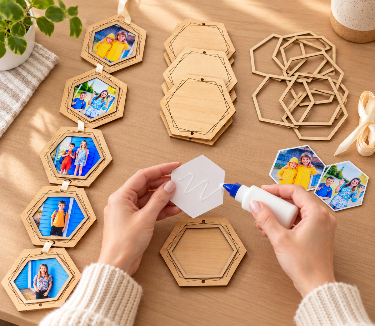 Hands applying glue to the back of a hexagon-shaped photograph, with wooden frame pieces and a finished photo garland arranged on a craft table.