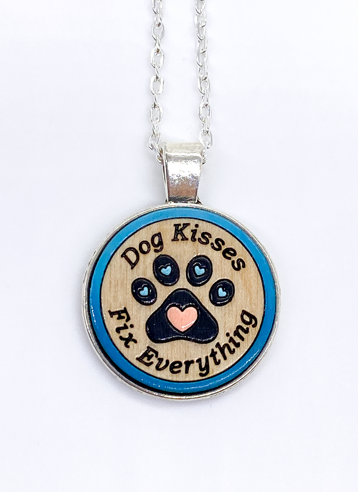 Hand-painted dog kisses necklace with engraved paw print on wood pendant, silver bezel, front view on white background