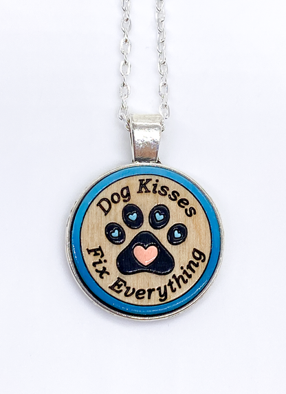 Hand-painted dog kisses necklace with engraved paw print on wood pendant, silver bezel, front view on white background