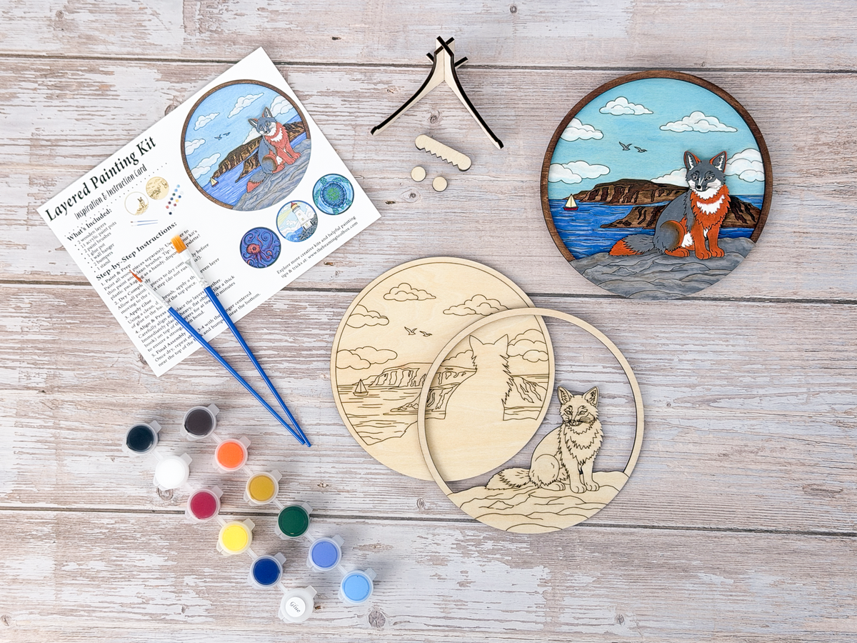 Fox Coastal layered wood painting kit with unfinished wood pieces, paint pots, brushes, display stand, packaging, and finished painted example.