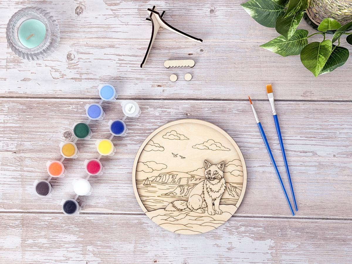 Unpainted Fox Coastal layered wood artwork displayed with paint pots, brushes, stand pieces, candle, and greenery on a rustic background.