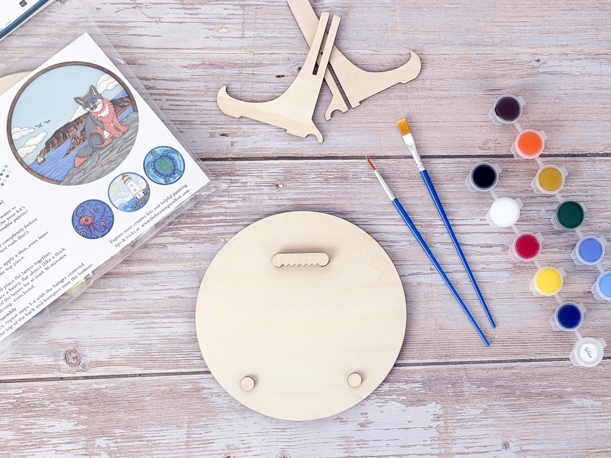 Back of the Fox Coastal wood craft kit showing the hanger piece, small bumpers, paint pots, brushes, display stand, and packaging.